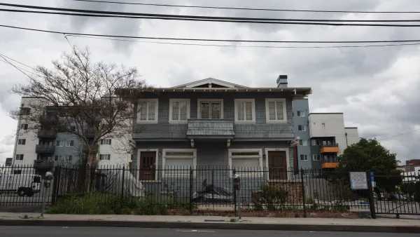 Grey two-story older home divided into two units inLos Angeles, California with modern apartment building visible in the background.