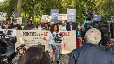 Crowd of activists protesting conditions at Rikers Island with one woman in front speaking into microphone