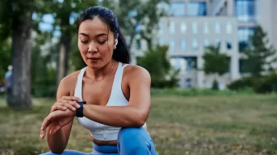 Woman sitting on grass with building in background, looking at her smart watch
