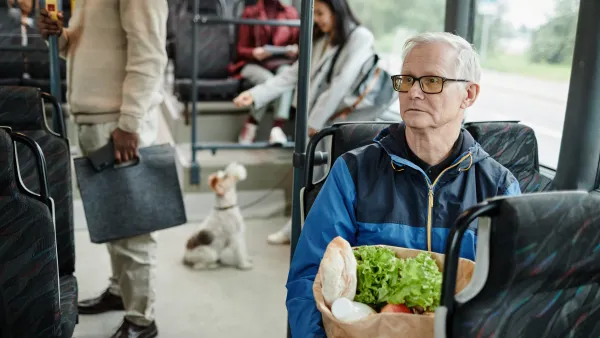 Elderly man holding a paper bag of groceries sitting on public bus.