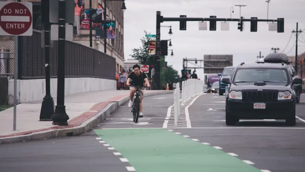 Man riding bicycle in protected green painted bike lane next to black SUV in Boston, Massachusetts.