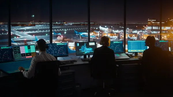 Three air traffic controllers sitting at their desks in a control tower at night.