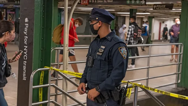 Police officer wearing black covid mask stands at top of staircase in New York City subway station.