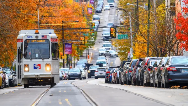 White SEPTA streetcar traveling down wide street in Philadelphia, Pennsylvania with fall foliage on trees on either side of street.