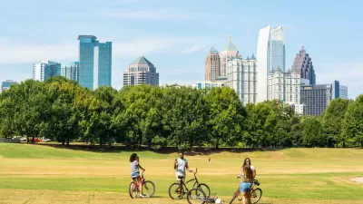Three people with bikes stopping to chat on grassy field with Atlanta, Georgia skyline in background