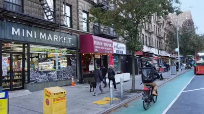 Cyclist rides down green-painted bike lane in Manhattan, New York next to small businesses with colored awnings