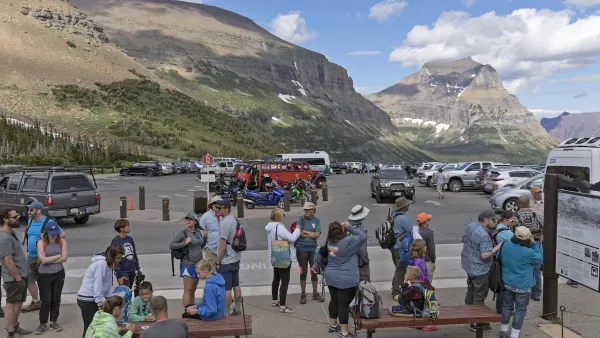 Large group of tourists wait in parking lot in Glacier National Park for park shuttle.