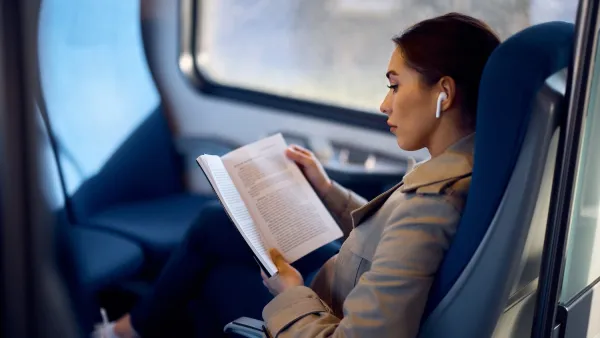 Woman reading book with white earbud in ear while sitting on train.