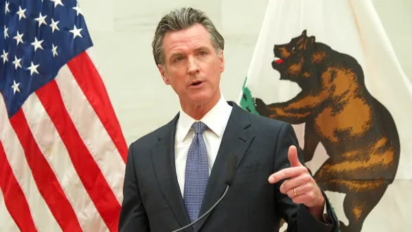 Gavin Newsom standing behind a podium, pointing at the camera. The flag of the United States and the flag of California are behind him.