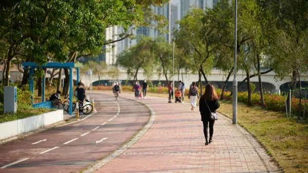 People walking on sidewalk adjacent to bike lane with trees and buildings in background in Hong Kong park