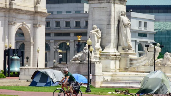 Cyclist rides past neoclassical buildings and homeless encampment in Washington, DC.