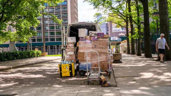 Delivery van parked on street in New York City with lots of packages stacked up outside the back door.