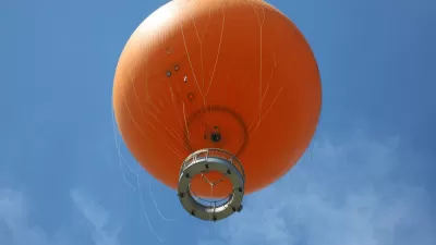 View from below of orange tethered hot-air balloon floating in blue sky