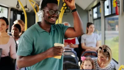Young man wearing headphones and holding a coffee cup standing on a city bus