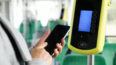 Close-up of person holding up smartphone next to contactless fare reading device on bus