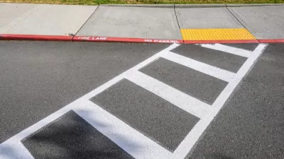 Freshly painted white crosswalk leading to yellow curb cut to sidewalk