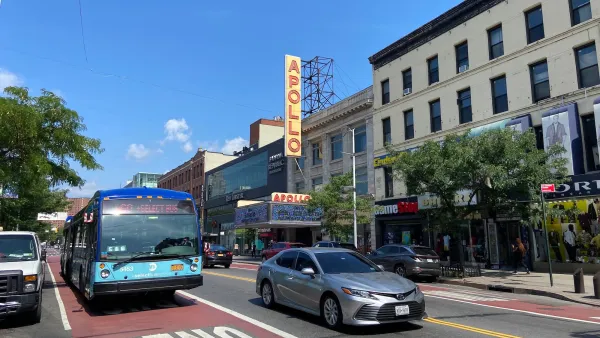 Red painted bus lane in New York City with marquee for Apollo theater in background.