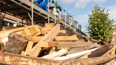 Old wood demolition waste, from destruction or renovation of buildings in a container on a work site in a street with a house. Wooden beams to be recycled into new building materials