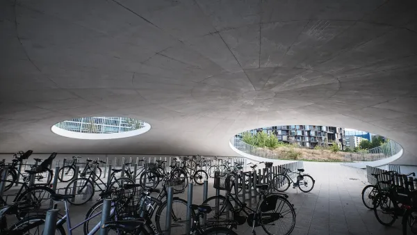 Partially underground concrete dome with circular openings and dozens of parked bicycles on University of Copenhagen campus.