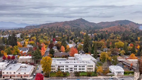 Aerial of Grants Pass, Oregon wth white city hall building in foreground and hills with colorfull fall leaves in background.
