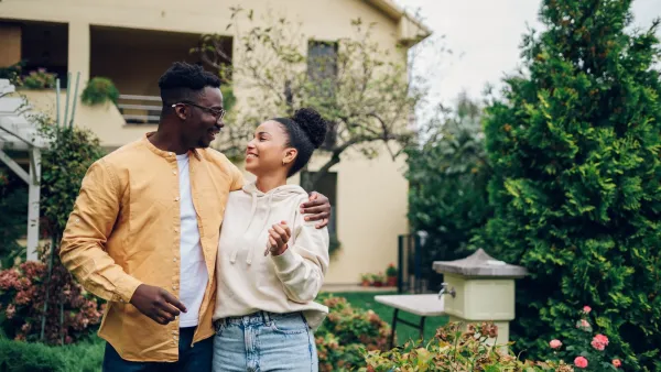 African American couple happily looking at each other in front of a two-story house.
