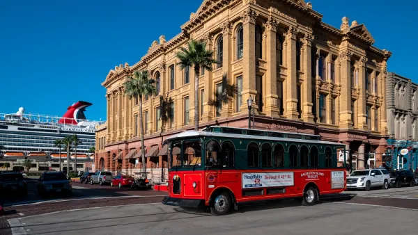 Historic turn of 20th century building in downtown Galveston, Texas with red streetcar passing by and large cruise ship visible in background.