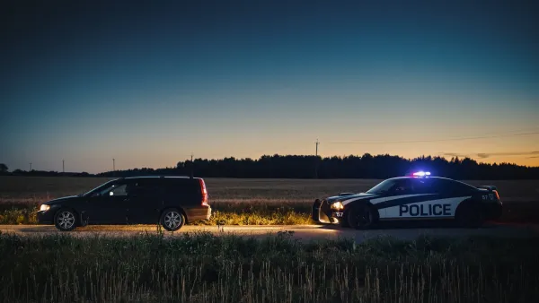 Police car pulling over dark station wagon on rural road at dusk.