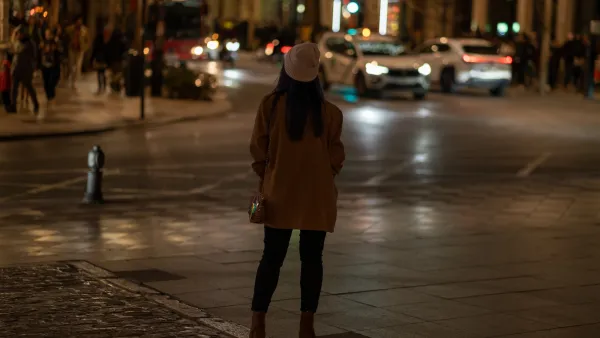 Back view of a woman in hat and coat standing on street in city at night.