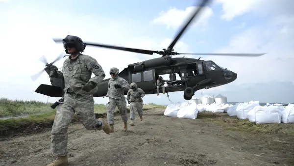 National Guard exiting a Black Hawk helicopter next to a pile of white sandbags during flood relief efforts.