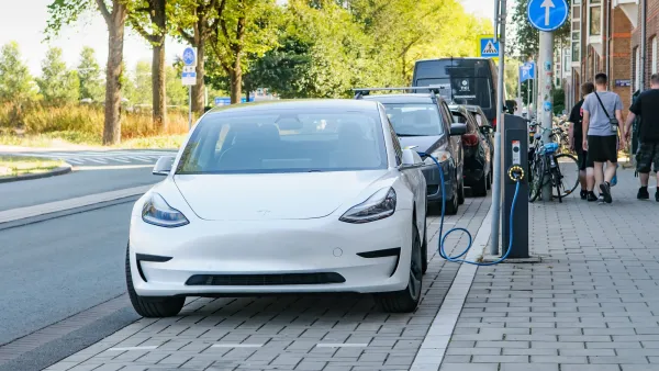 White Tesla plugged into curbside electric car charger on street in Amsterdam, Netherlands.