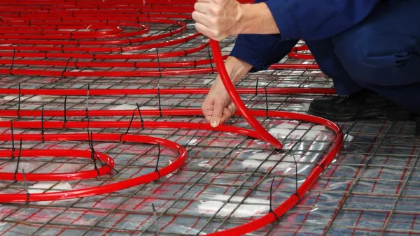 A person lays down red geothermal pipes.