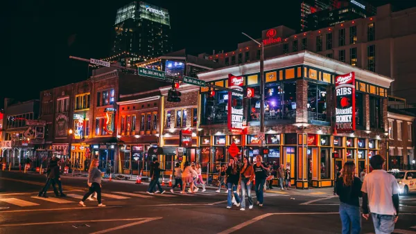 People walking on Broadway street with neon signs for bars and music venues in Nashville, Tennessee.