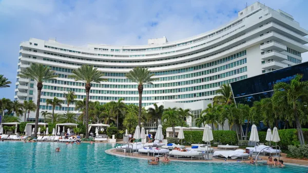 Large white curved hotel building with pool and white poolside chairs and umbrellas in Miami Beach, Florida.