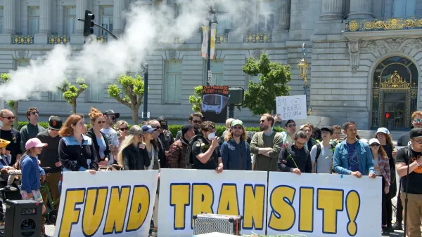 People rallying in front of government building in San Francisco holding "FUND TRANSIT!" sign.