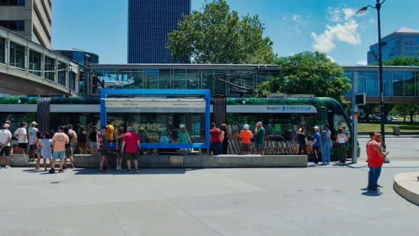Crowd of people stand at station in front of blue and green Kansas City streetcar.