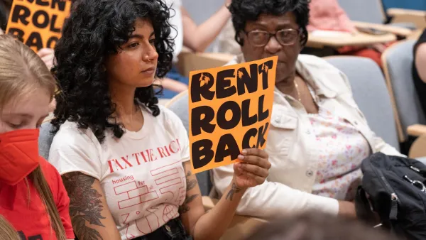 Young woman holding up "RENT ROLL BACK" sign in public meeting.