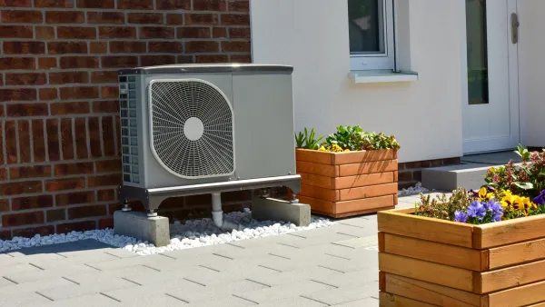 Heat pump installed next to brick wall on  residential building next to brown wood planter boxes.