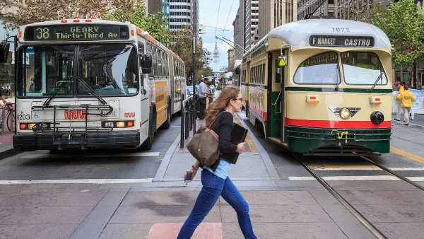Woman in jeans and blue flats walks across a street in San Francisco with a vintage streetcar and a bus behind her.