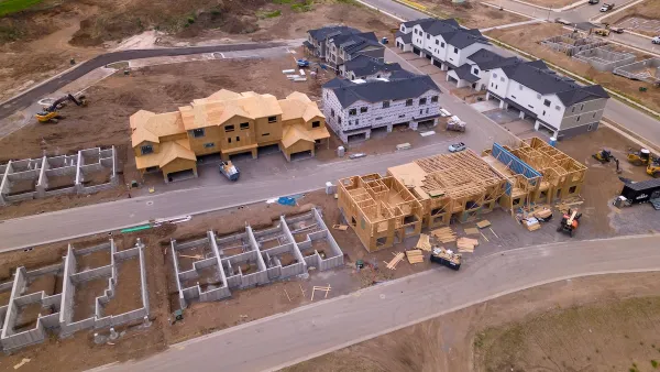 Aerial of wood-framed homes under construction in cleared dirt lots.
