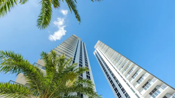 Looking up at modern high-rise buildings with palm trees in foreground against bright blue sky in Miami, Florida.