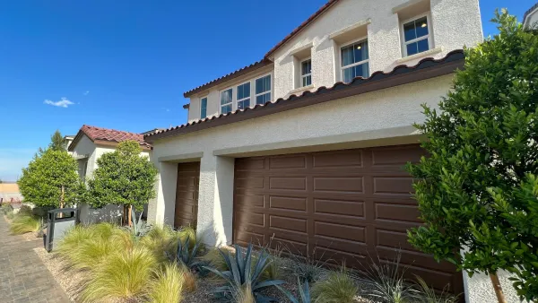 Neo-Spanish style new house with brown garage door and xeriscaped small yard.