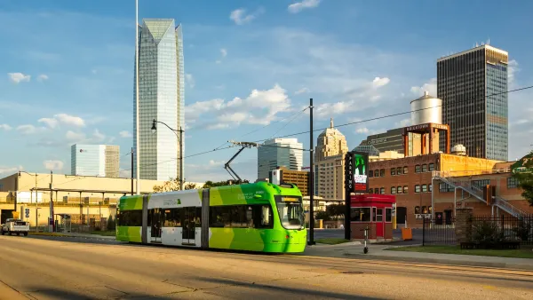 Green Oklahoma City streetcar with downtown skyline in background.