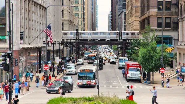 Bustling intersection with pedestrians, transit buses, and a train passing on an elevated rail above in downtown Chicago, Illinois.