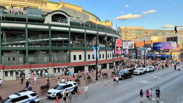 Wrigley Field, Chicago with two white police SUVs parked on street outside with people walking around.