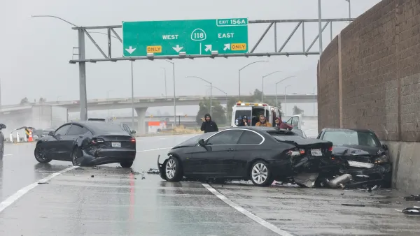 Three black cars crashed into each other on a rainy freeway under green exist signs with police officers standing next to cars.