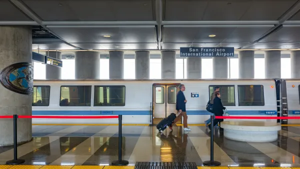 Two people walking in front of stopped BART train at station in San Francisco Bay Area.