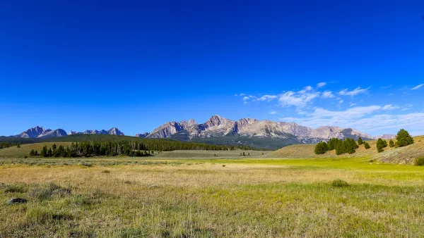 Public land in Idaho. Most of the photo is a green field, with mountains and a forest in the distance.