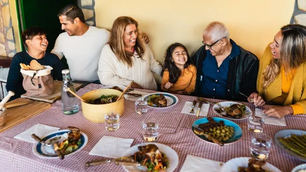 Happy family sitting at table with checkered red and white tablecloth and multiple plates and bowls of food.