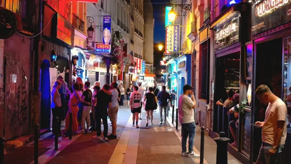 People walking in an alley with neon signs for ice cream shops and stores at night in the Latin Quarter, Paris, France.