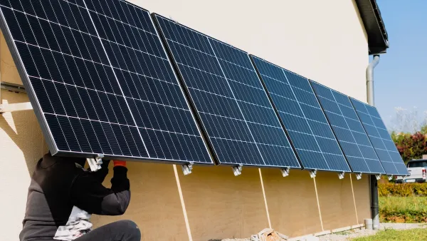 A person installing solar panels on a wall. The panels are tilted slightly, the head of the person is hidden under one of them.